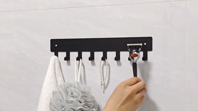 Svart självhäftande kroklist med badrumstillbehör på en kaklad vägg.